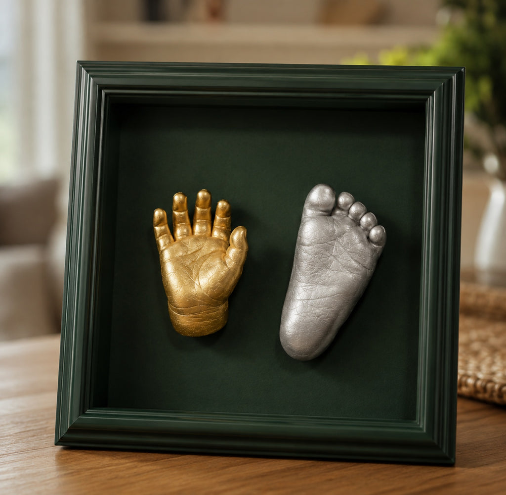 Finished gold hand and silver foot baby casts displayed in a green shadow-box frame