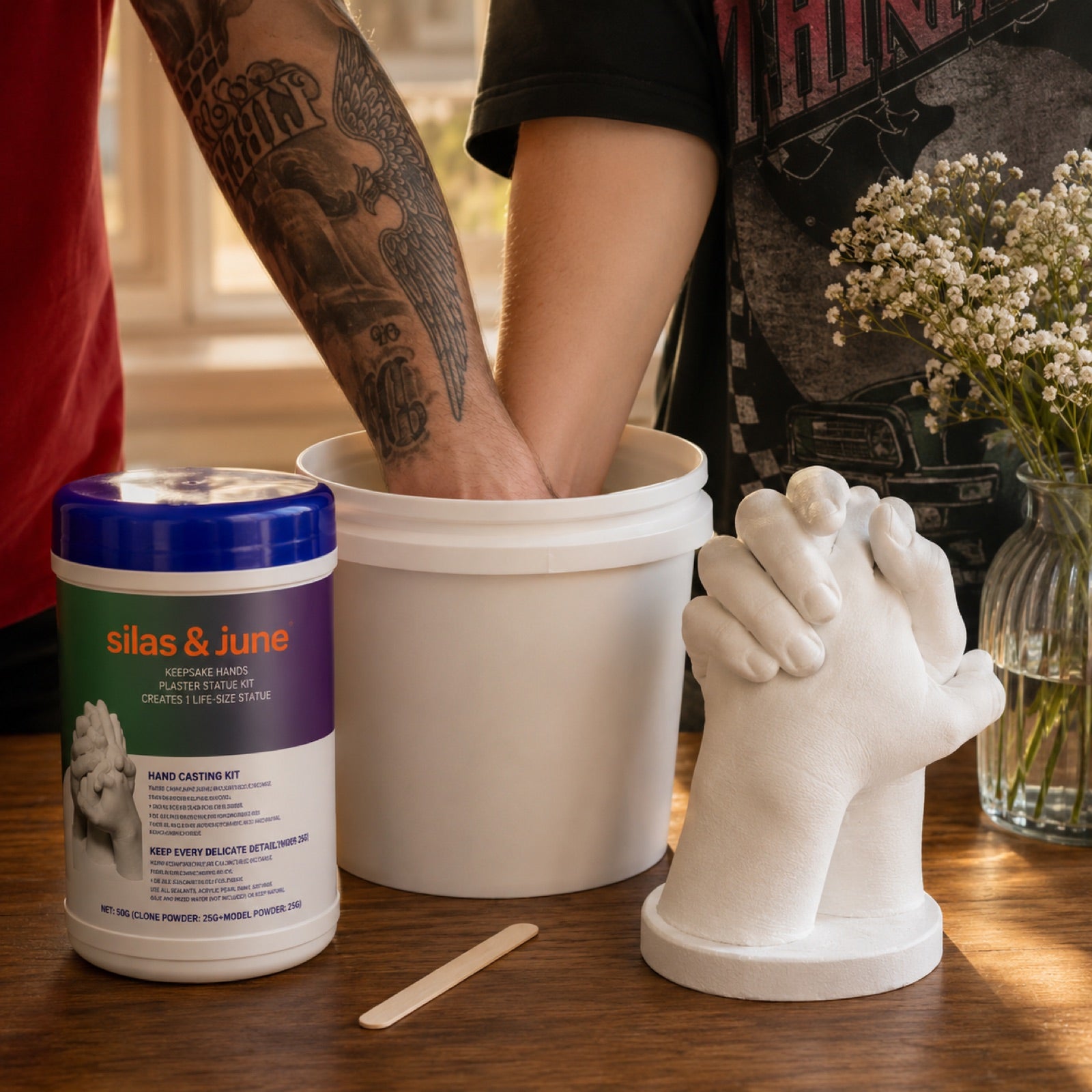 Couple making a hand casting keepsake, hands in the molding bucket beside the finished clasped-hands statue